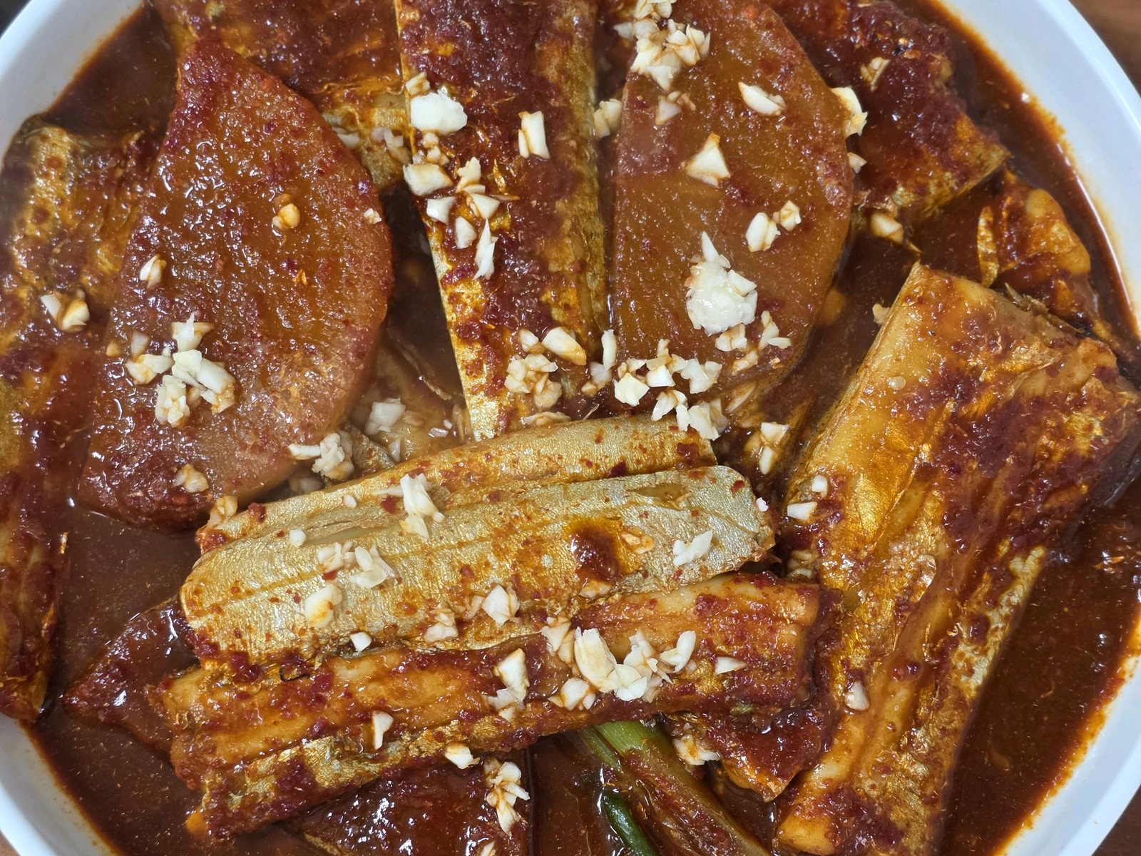 성심조림 제주공항점 제주마농 갈치조림 — 위에서 본 한 그릇, 갈치 토막과 무, 대파, 다진 마늘이 붉은 양념에 잠겨 있다.