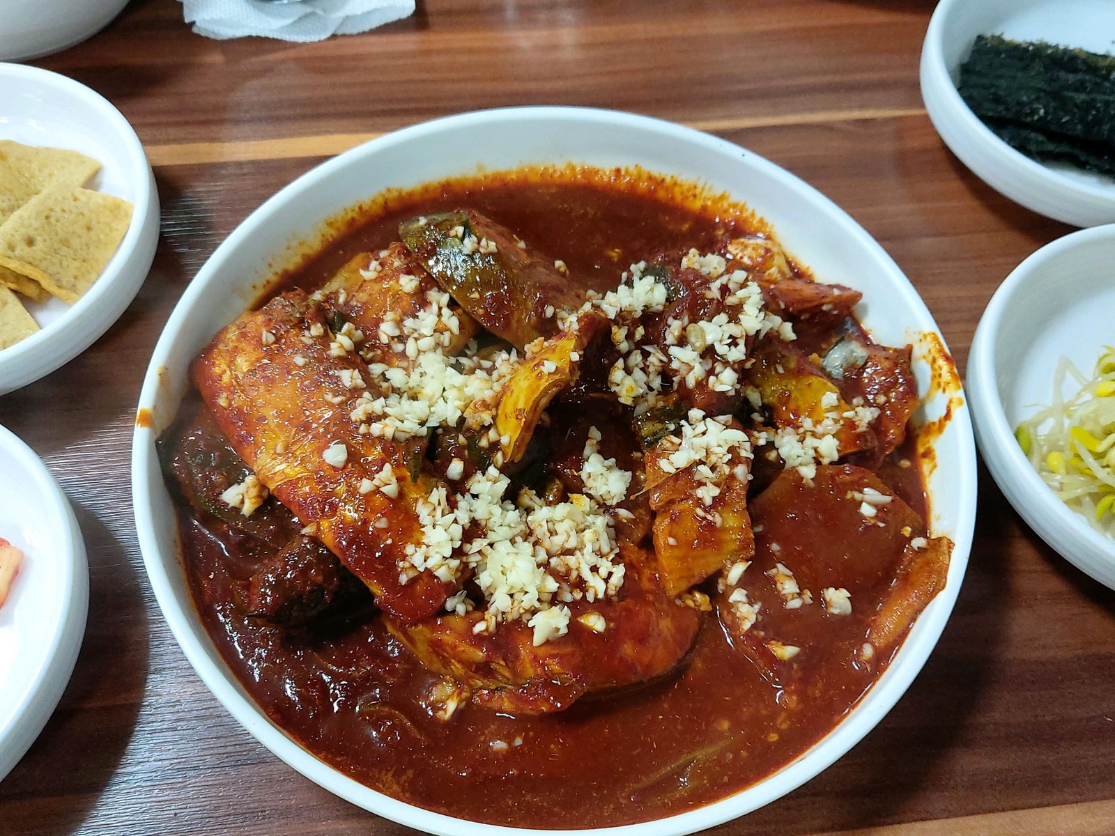 성심조림 제주공항점 조림 한 상 — 짙은 원목 식탁 위 다진 마늘을 올린 조림 한 그릇과 반찬, 된장국, 냅킨 위 수저.