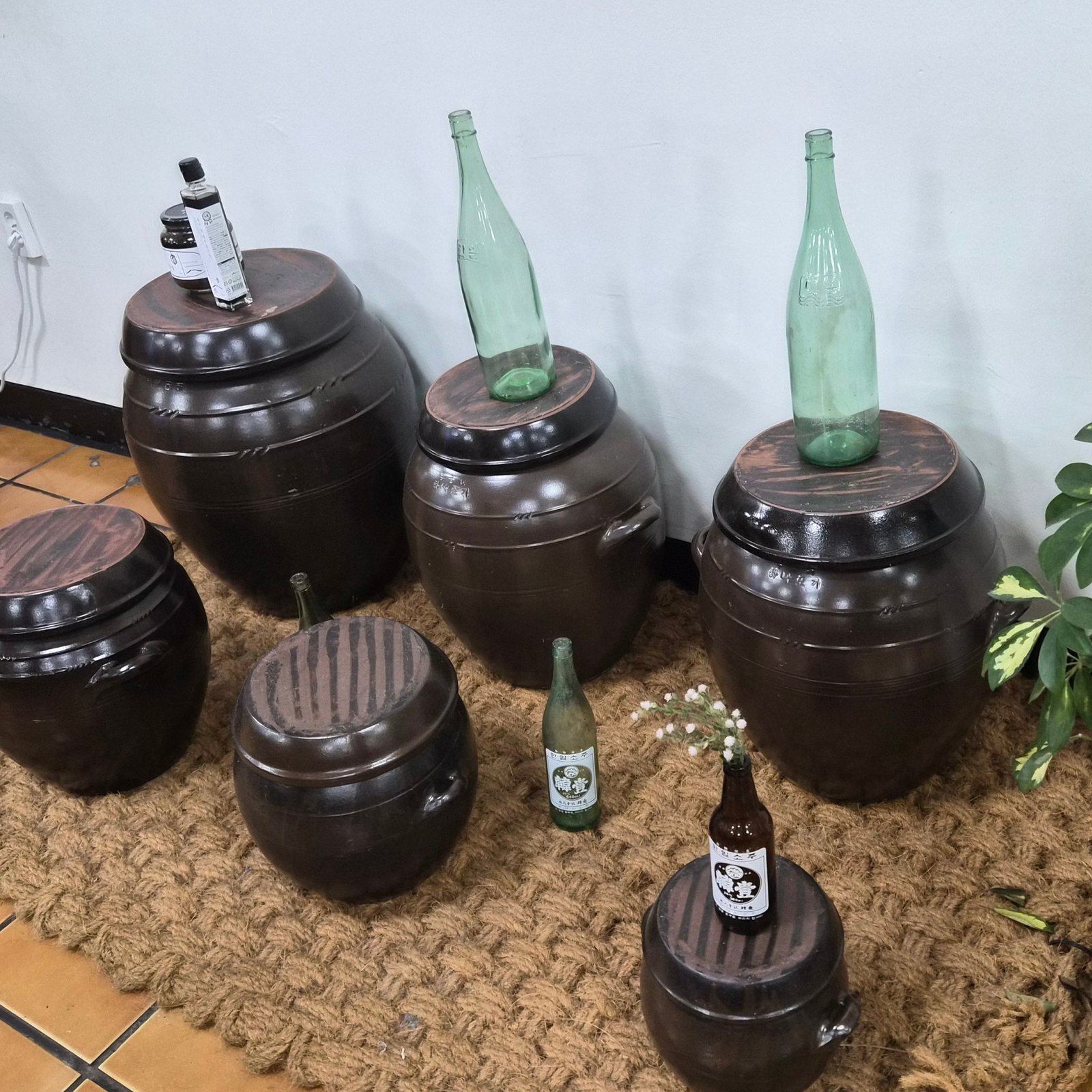성심조림 제주공항점 매장 — 입구 쪽 야자 매트 위에 늘어놓은 짙은 갈색 옹기 항아리들과 초록 유리 됫병.