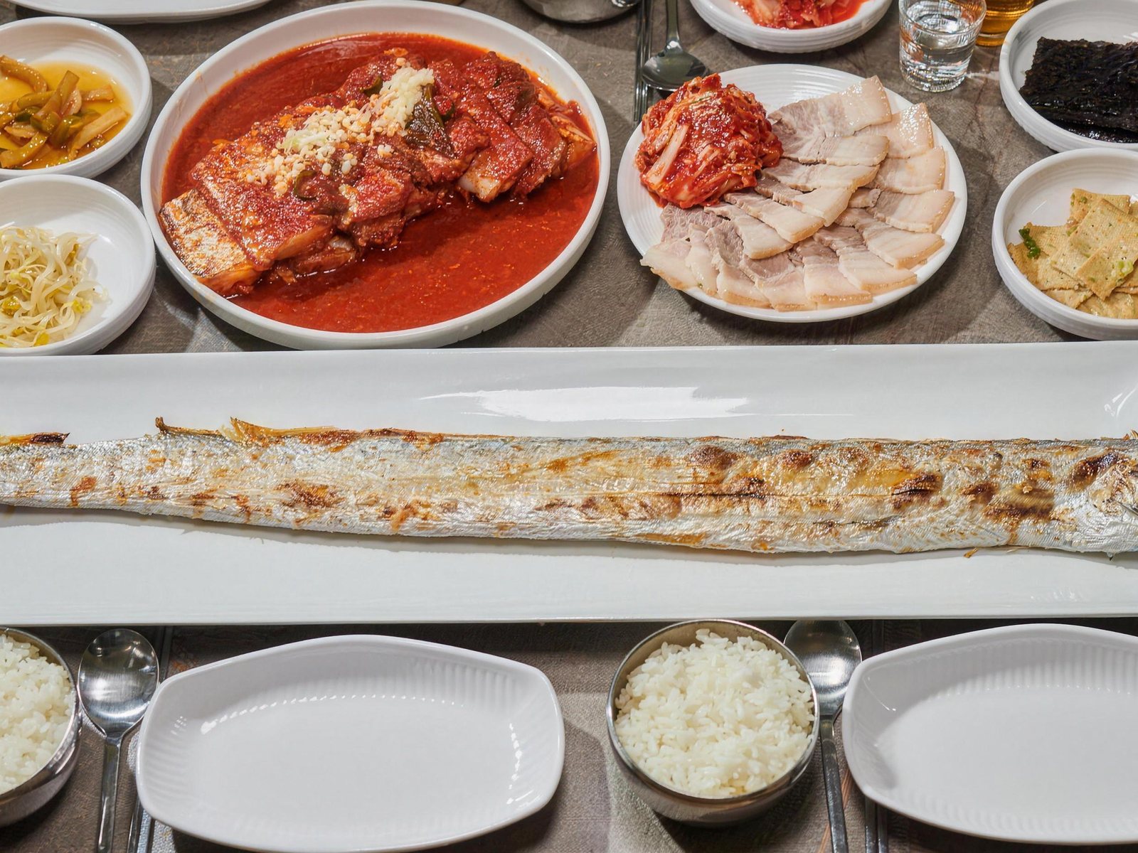 성심조림 제주공항점 한 상 차림 — 위에서 내려다본 긴 흰 접시의 통갈치구이 한 마리, 다진 마늘을 올린 갈치조림, 겉절이와 수육, 장아찌·콩나물·김·어묵볶음 반찬과 공기밥.