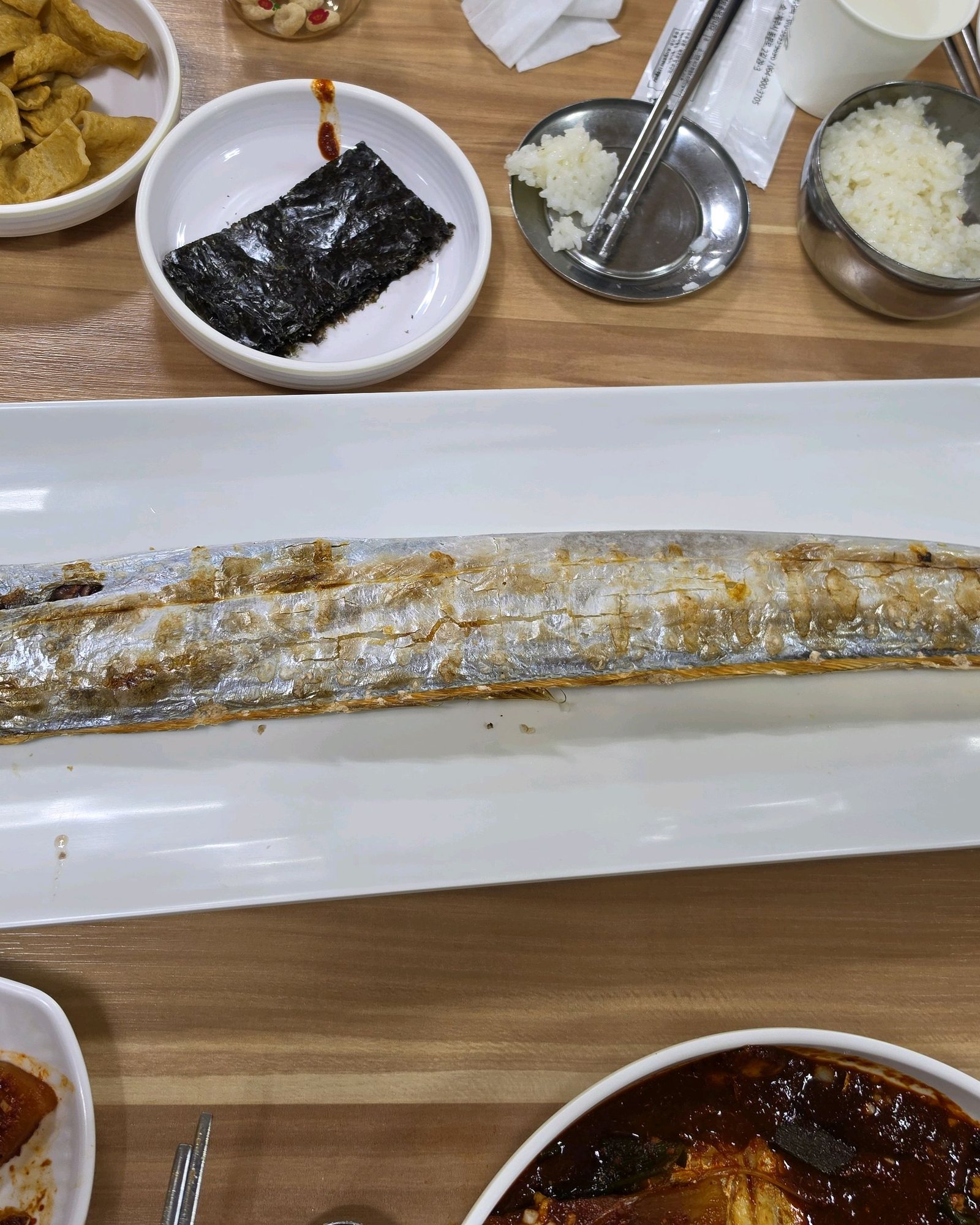 성심조림 제주공항점 통갈치구이 — 긴 흰 접시에 갈치 한 마리를 통째로 구워 올렸고, 위로 장아찌·김·어묵 반찬과 공기밥.